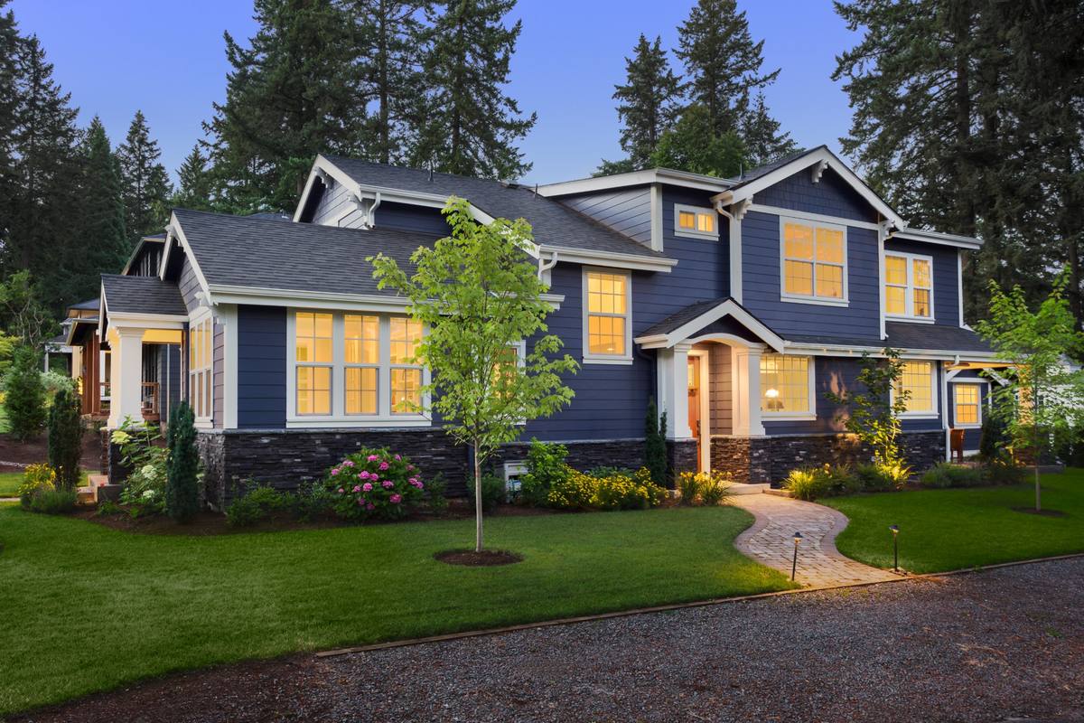 Blue two-story home at dusk with lit windows, porch lights and pathway lights