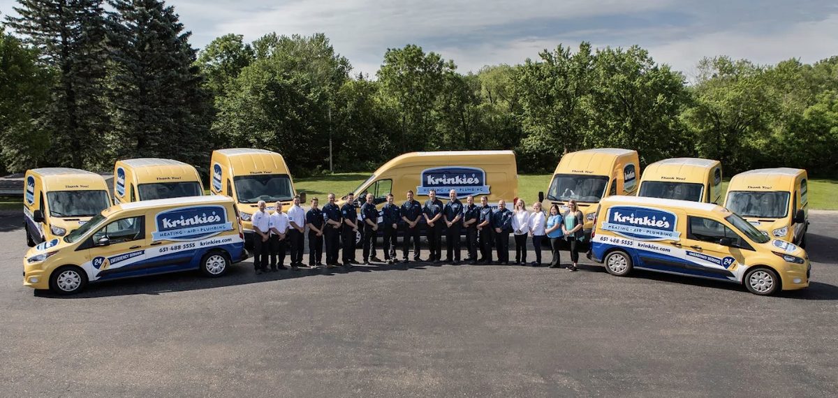 The Krinkie’s Heating, Air and Plumbing team standing in a row between their yellow and blue service vans
